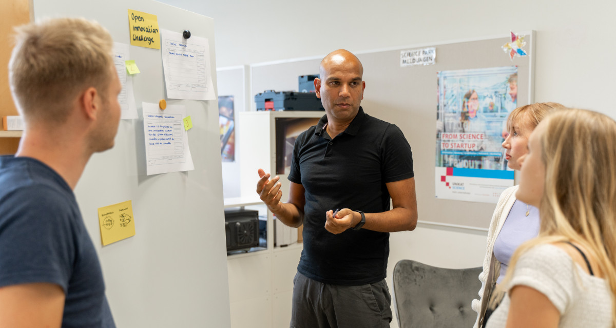 Science Park Coach Stefan Rötzel erklärt drei Personen etwas an einer Pinnwand.