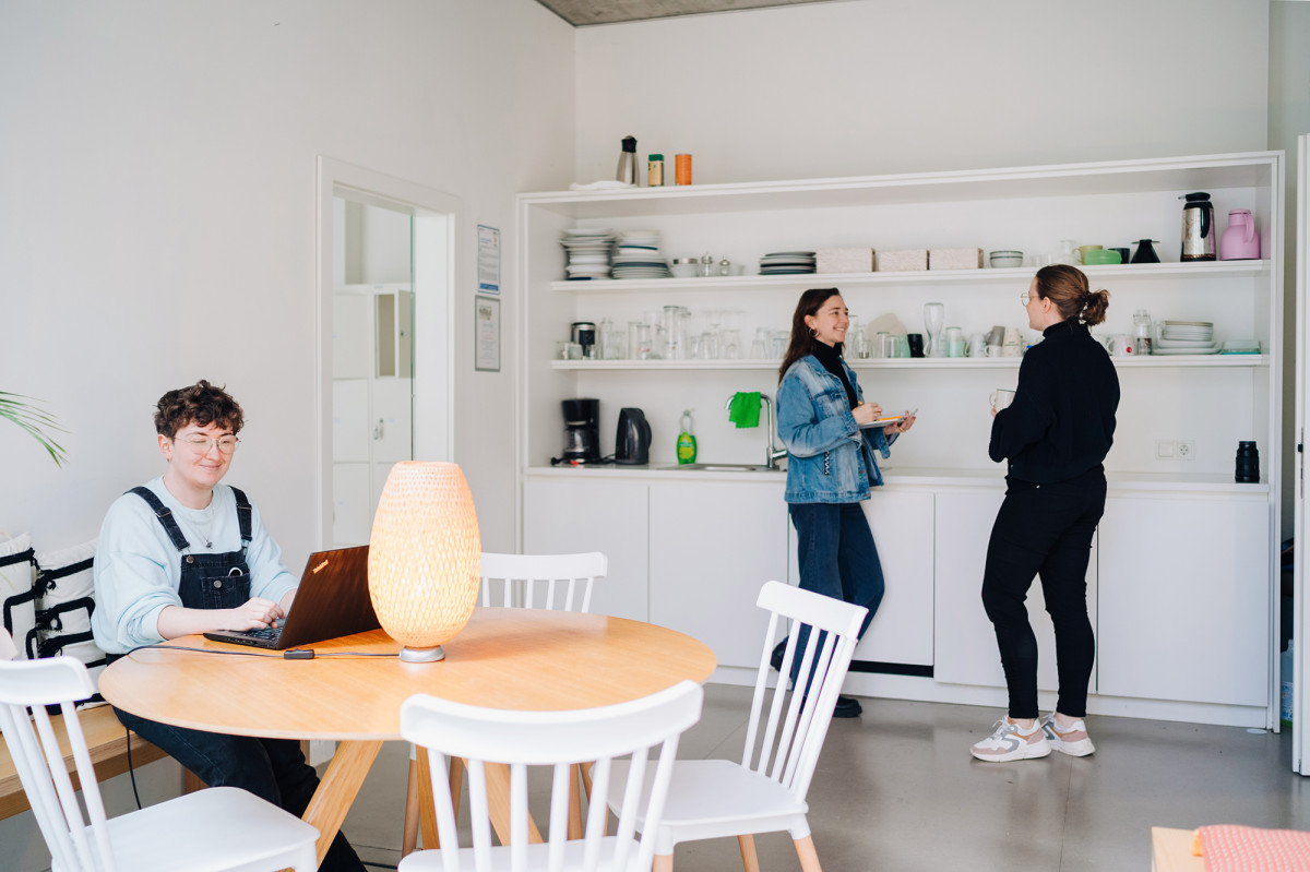 Junge Menschen arbeiten im CoWorking Bereich und unterhalten sich in der gemütlichen Küche